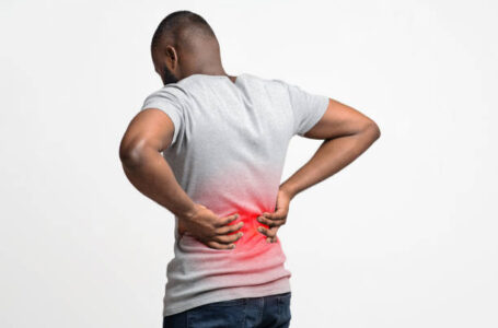 Afro guy holding both hands on lower back, pain in spine, inflamed zone highlighted in red, white background, free space